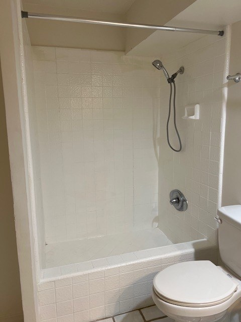 A white toilet is in a bathroom with a white tiled shower.